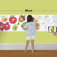 The image depicts a father and his two daughters enjoying a bonding moment while colouring fruits sheet attached to the wall.